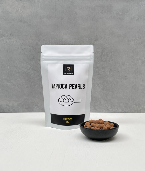 Resealable pouch holding 3 servings of Brown Tapioca Pearls. Displayed with uncooked Brown pearls in a black ceramic dish