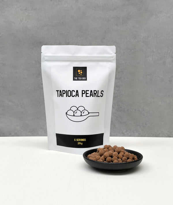 Resealable pouch holding 6 servings of Brown Tapioca Pearls. Displayed with uncooked Brown pearls in a black ceramic dish