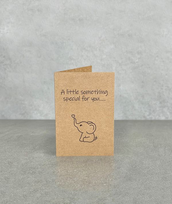 Brown kraft card, titled “A Little Something Special For You”. Drawing of a baby elephant staring at a small love heart floating in the sky above its trunk. Folded card is 70 x 100 mm