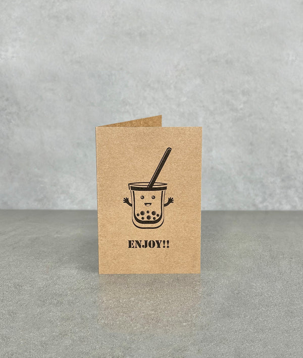 Brown kraft card, titled “Enjoy!!”. Shows a cartoon bubble tea character smiling with arms waving. Card measures 70 x 100 mm when folded