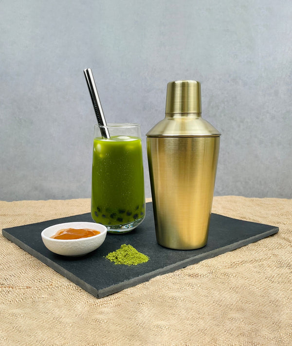 Brushed gold shaker displayed with Matcha Yuzu bubble tea with Blueberry pearls, silver stainless steel straw, Matcha powder and Yuzu fruit mix