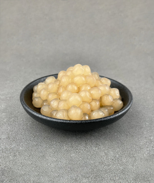 Cooked, off-white Lychee tapioca fruit pearls in a small black ceramic dish