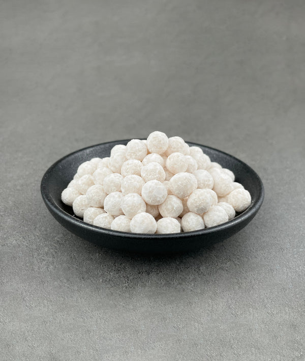 Uncooked Lychee tapioca fruit pearls in a small black ceramic dish