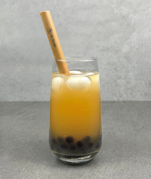 A glass of Lychee Bubble Tea with Blueberry pearls, ice and a reusable bamboo bubble tea straw