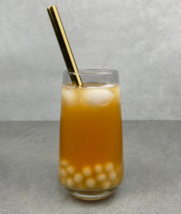 A glass of Lychee and Passionfruit Bubble Tea with Yuzu pearls, ice and a gold stainless steel straw