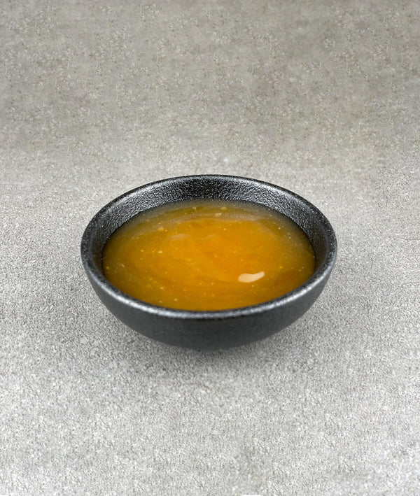 Small black ceramic dish filled with light orange Lychee and Passionfruit fruit mix