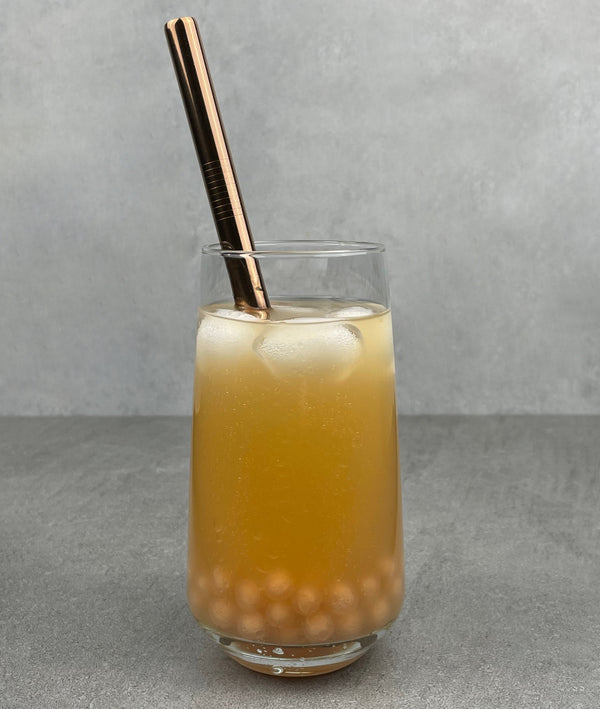 A glass of Lychee Bubble Tea with Red Grapefruit tapioca fruit pearls, ice and a rose gold stainless steel bubble tea straw