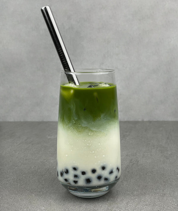 A glass of cold Matcha Latte Bubble tea with Blueberry pearls, ice and a silver stainless steel bubble tea straw