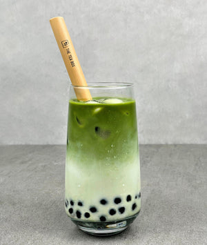 A glass of cold Matcha Latte Bubble tea with Blueberry pearls, ice and a reusable bamboo bubble tea straw