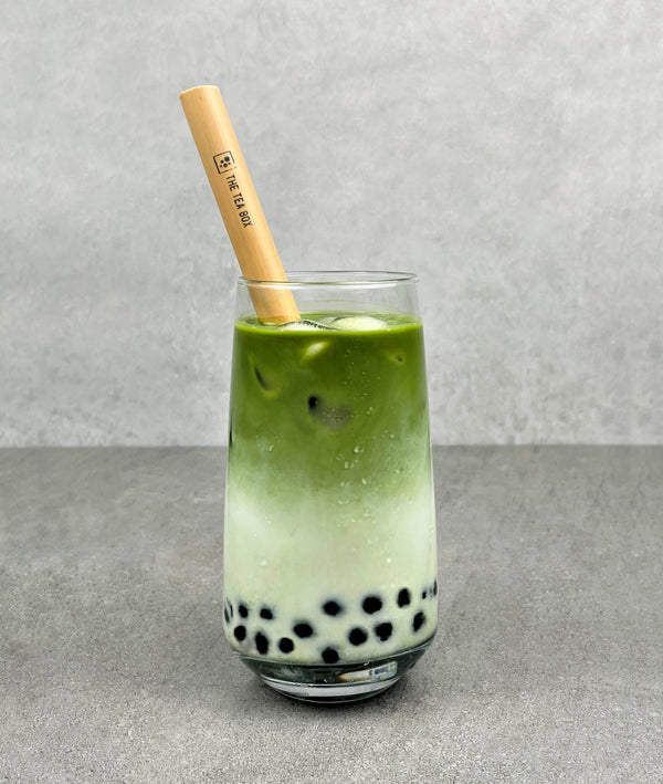 A glass of cold Matcha Latte Bubble Tea with Blueberry tapioca fruit pearls, ice and a reusable bamboo bubble tea straw