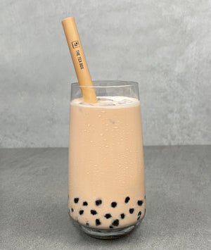 A glass of Pearl Milk Bubble tea with brown tapioca pearls, ice and a reusable bamboo bubble tea straw