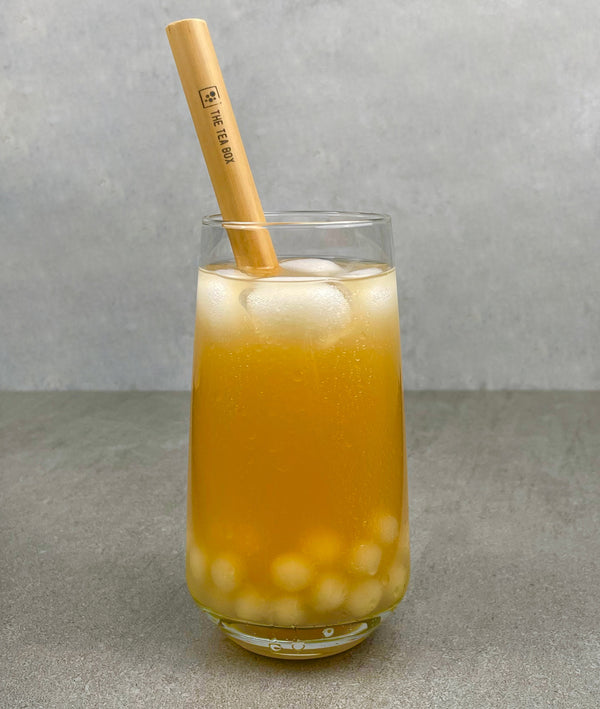 A glass of Passionfruit Bubble Tea with Pineapple tapioca fruit pearls, ice and a reusable bamboo bubble tea straw