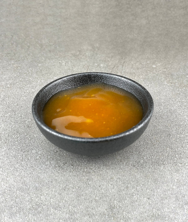Small black ceramic dish filled with orange-coloured Passionfruit fruit mix