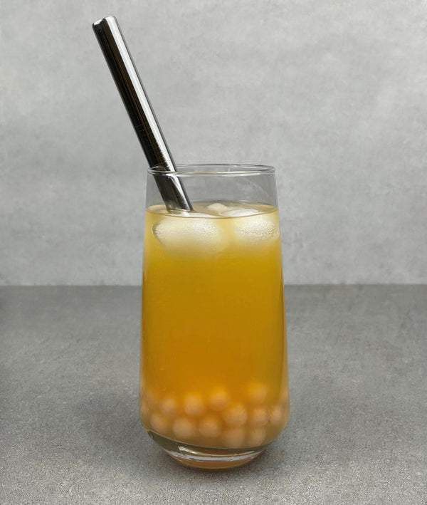 A glass of Passionfruit Bubble Tea with Red Grapefruit pearls, ice and a silver stainless steel straw