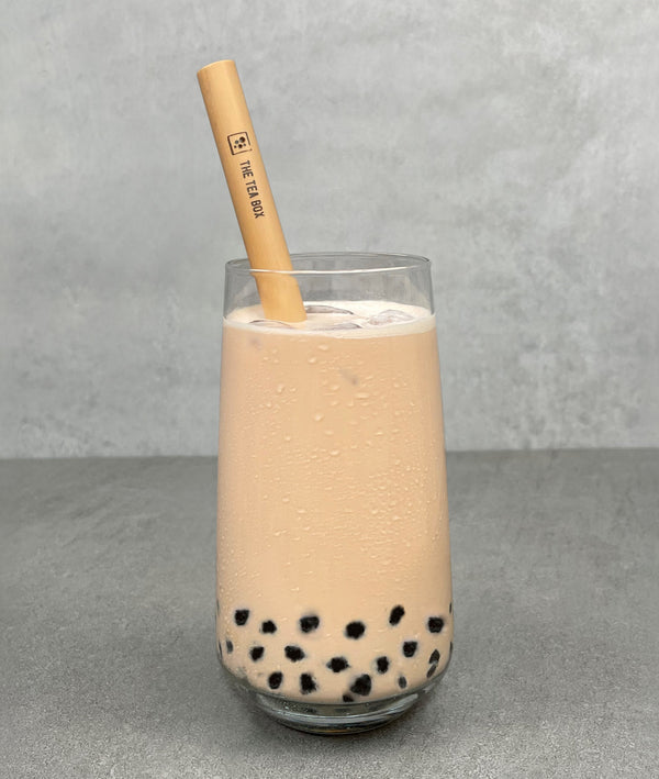 A glass of Pearl Milk Bubble Tea with Brown tapioca pearls, ice and a reusable bamboo bubble tea straw
