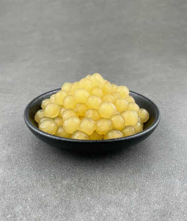 Cooked, yellow Pineapple tapioca fruit pearls in a small black ceramic dish