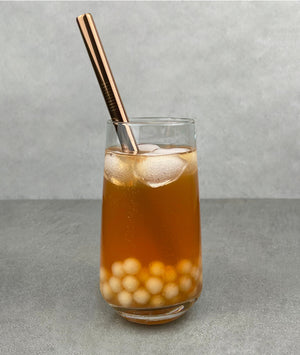 A glass of Red Grapefruit Bubble Tea with Yuzu pearls, ice and a rose gold stainless steel straw
