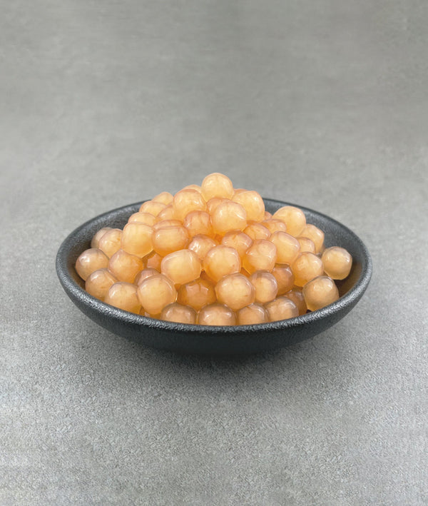 Cooked, pink-coloured Red Grapefruit tapioca fruit pearls in a small black ceramic dish