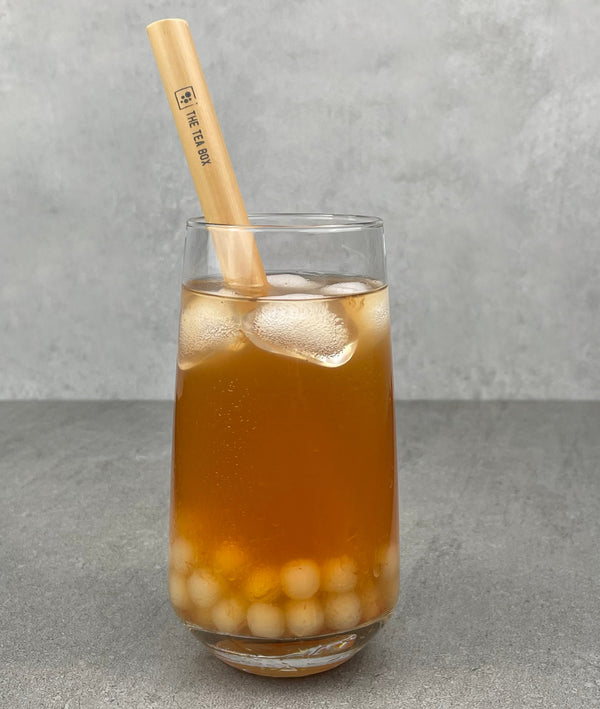 A glass of Red Grapefruit Bubble Tea with Lychee tapioca fruit pearls, ice and a reusable bamboo bubble tea straw