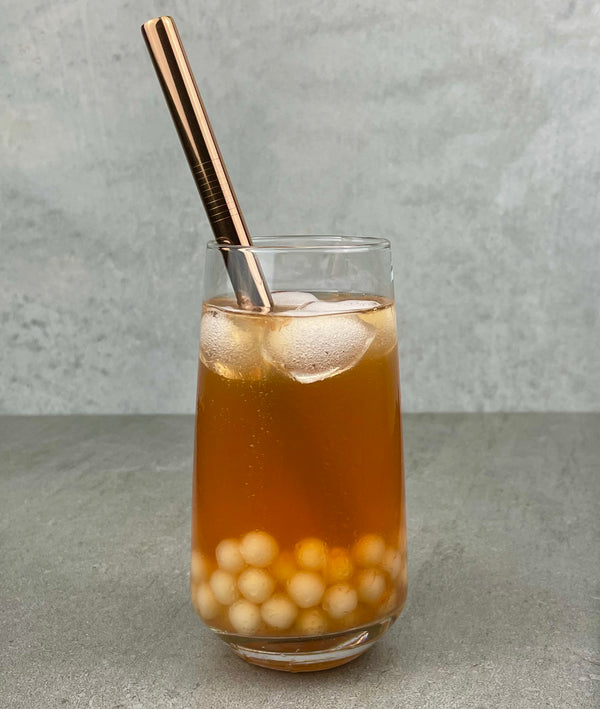 A glass of Red Grapefruit Bubble Tea with Yuzu tapioca fruit pearls, ice and a rose gold stainless steel bubble tea straw