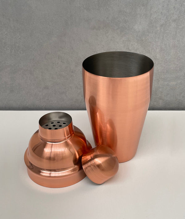 Unassembled rose gold 3-piece shaker with a shiny brushed finish in traditional cobbler style. Showing the cup, strainer and cap