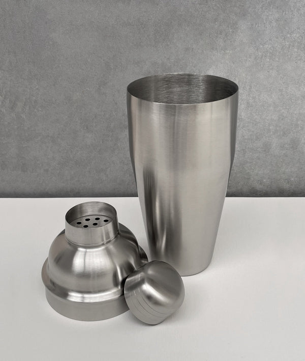 Unassembled silver, brushed stainless steel 3-piece shaker in traditional cobbler style. Showing the cup, strainer and cap