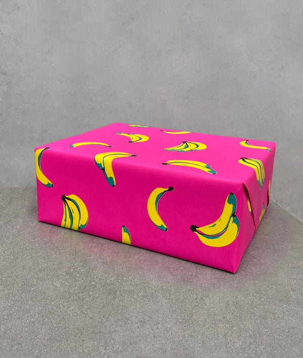 Bananas gift wrapping paper. Bright pink background covered in yellow and metallic green bananas