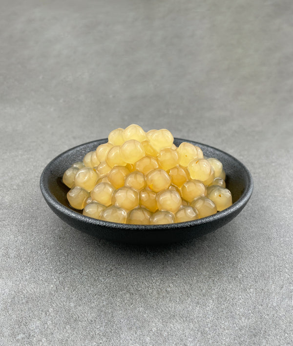 Cooked, yellow Yuzu tapioca fruit pearls in a small black ceramic dish