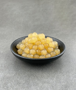 Cooked yellow Yuzu tapioca fruit pearls in a small black ceramic dish